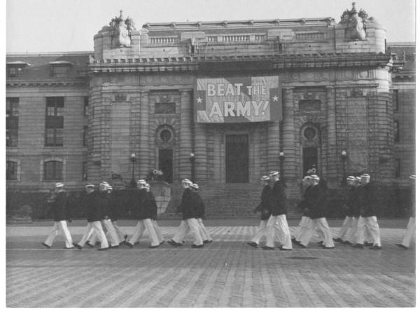 Midshipman marching across the front of rotunda of Bancroft Hall at the Naval Academy, with a 'Beat Army' sign as backdrop. Fall of 1938.